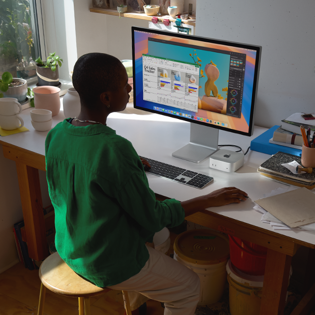 En person vid ett skrivbord som använder en Mac mini med skärm till att arbeta i appar som fyller skärmen med färger